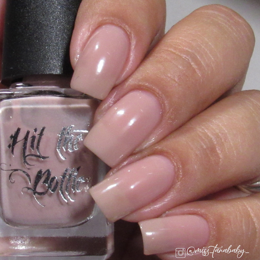 Hand holding a bottle of 'Hit the Bottle' nail polish with a neutral nail color.