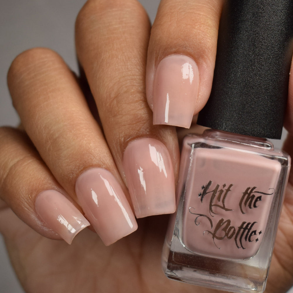 Hand with  nude pink nail polish holding a bottle of 'Hit the Bottle' nail polish.