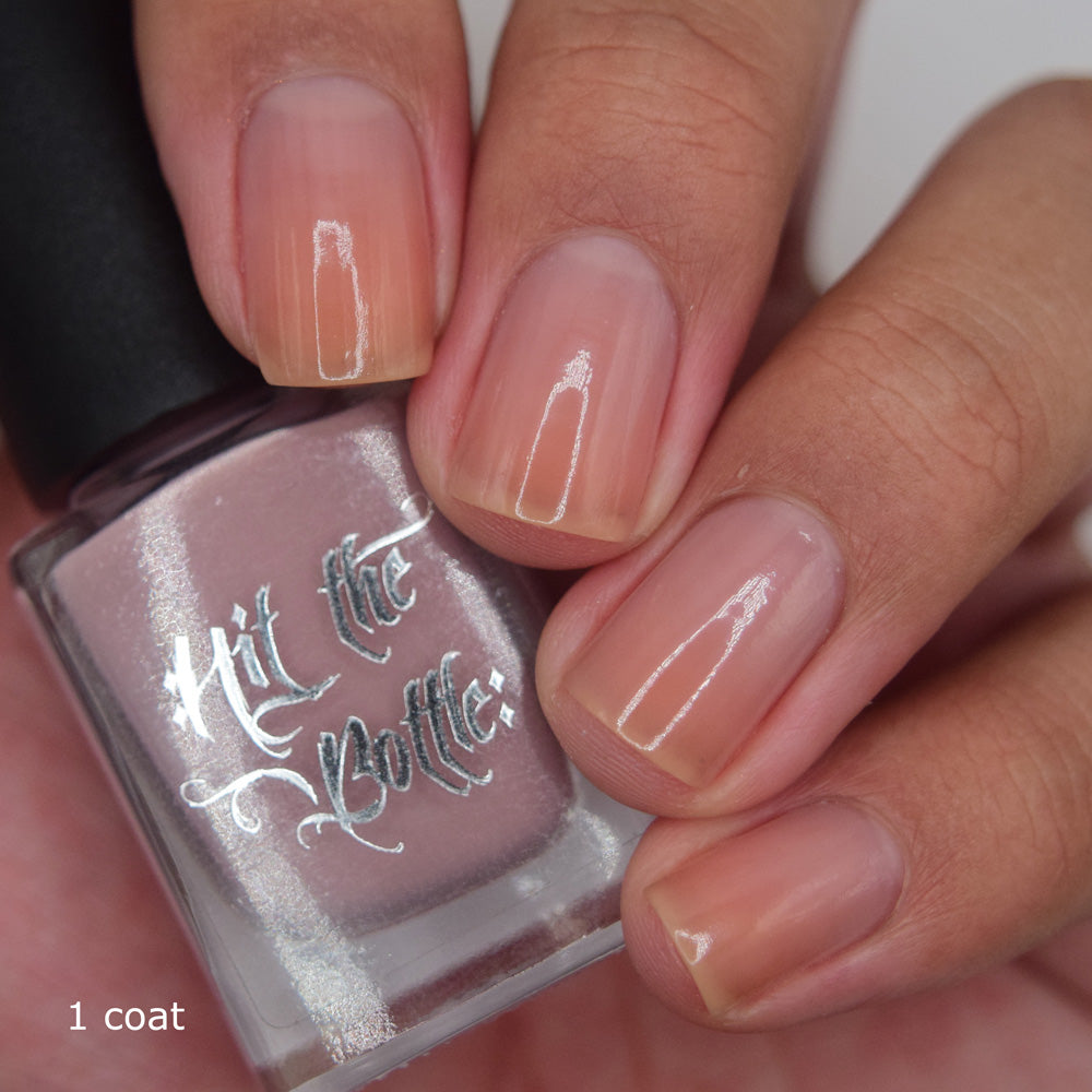 Nail polish bottle with 'Hit the Bottle' text held by a hand with painted blush pink nails.