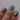 Close-up of a hand with green glittery nail polish on a gray background