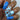 A close-up of a hand showcasing a manicure with glossy medium blue nails and a light blue accent nail decorated with orange pumpkins and black script reading 'Sweet and Scary'.