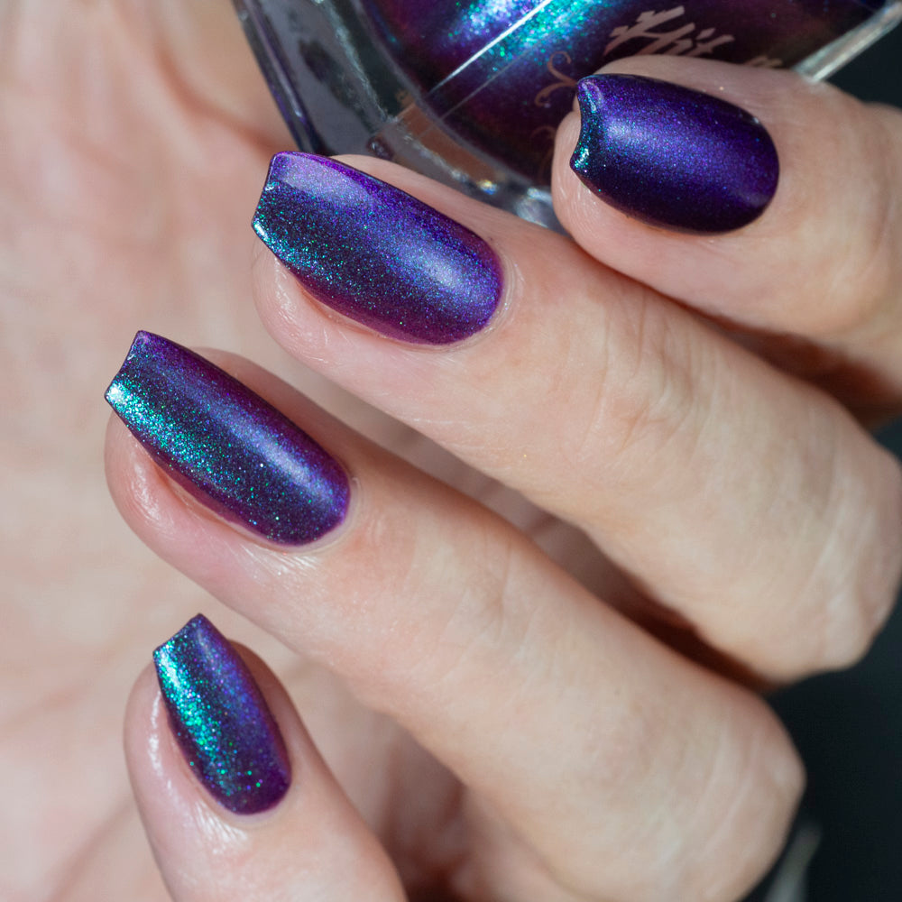 Hand with purple glittery nail polish holding a purple bottle.