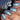 Close-up of manicured fingernails with a blue and iridescent green floral pattern, shown next to a dark nail polish bottle.