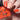 Close-up of a hand showcasing orange nail polish from the brand 'Hit the Bottle', with three nails painted in solid matte orange and one white nail decorated with orange scissors patterns.