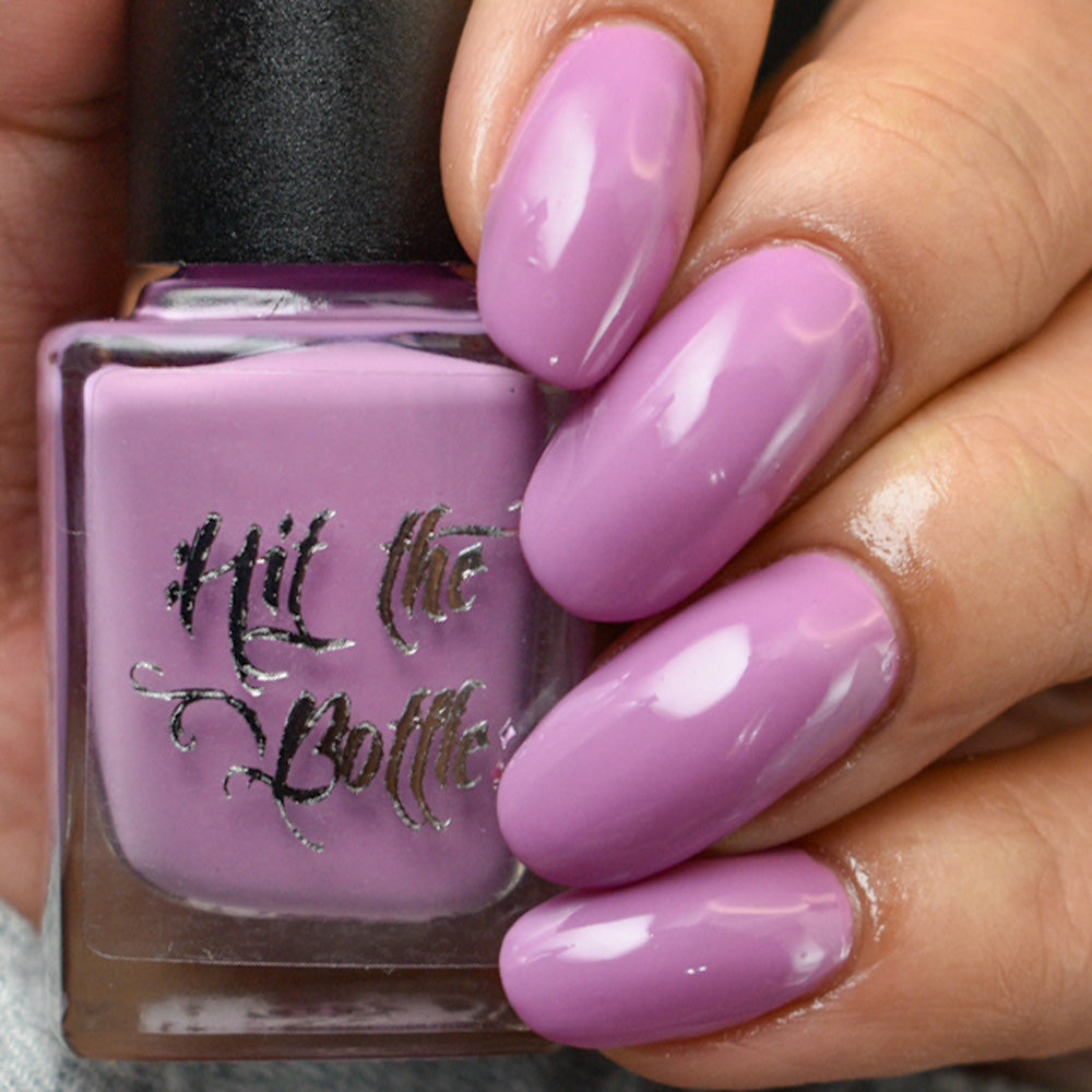 Hand holding a bottle of 'Hit the Bottle' nail polish with matching pink nails.