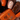 Close-up of a hand with orange and black nail art holding an orange nail polish bottle.