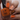 Hand with orange nail polish holding a bottle of 'Hit the Bottle' nail polish.