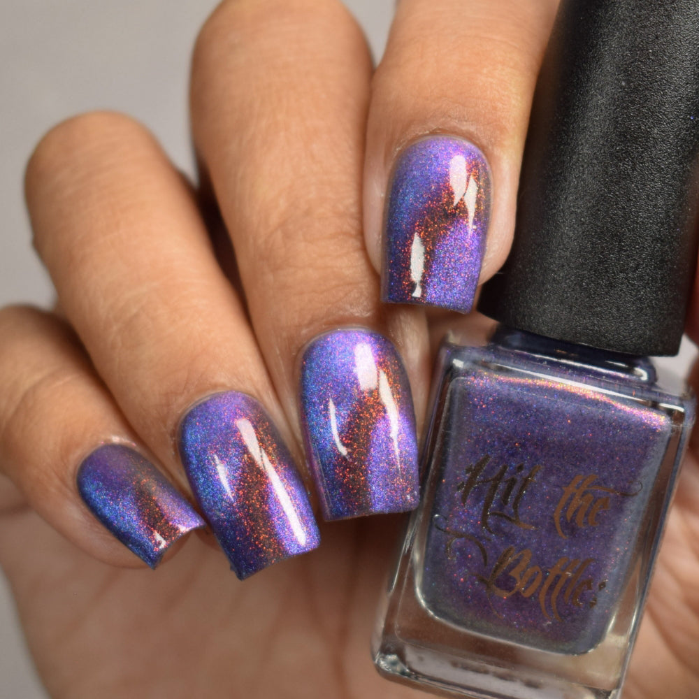 Nail polish with a metallic purple finish held by a hand, next to a bottle labeled 'Hit the Bottle'.