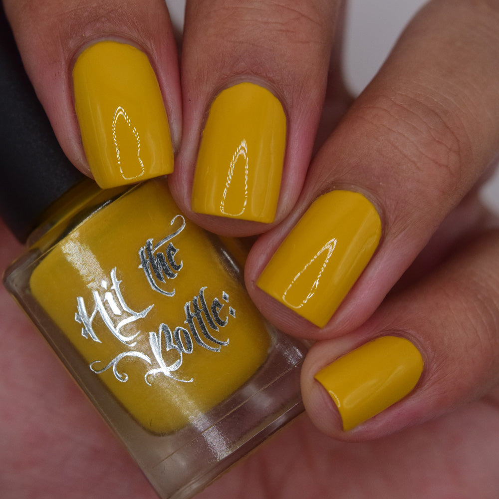 Mustard nail polish bottle held by a hand with matching nails.