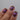 Close-up of a hand with purple and gold glittery nail polish on a gray background