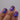 Close-up of a hand with purple glittery nail polish on a gray background
