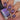 Nail polish with glittery purple and red design on nails, held by a hand.