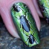 Green polish base, gold flake topcoat. Beetles stamped in silver and then black.  Macro photo of one nail.  Close up. 